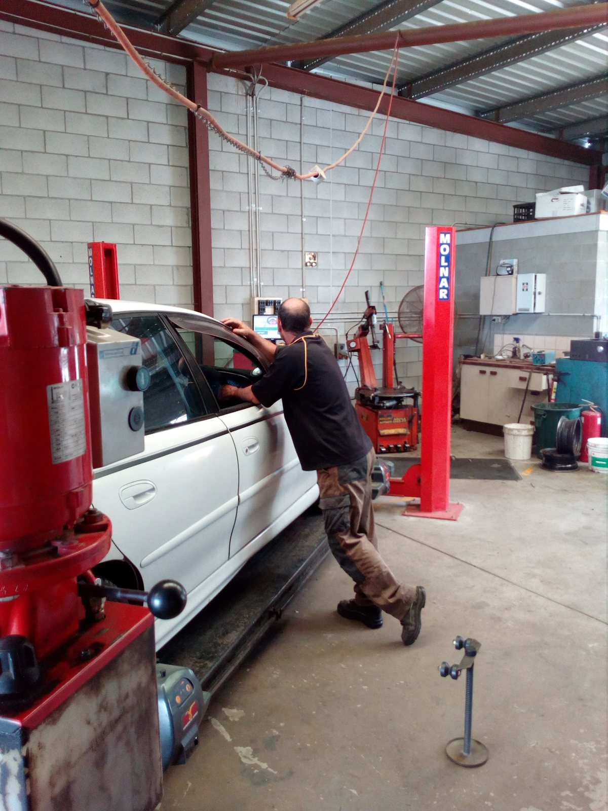 Technician working on a white sedan beside the hoist and tyre changer inside the Brendale workshop