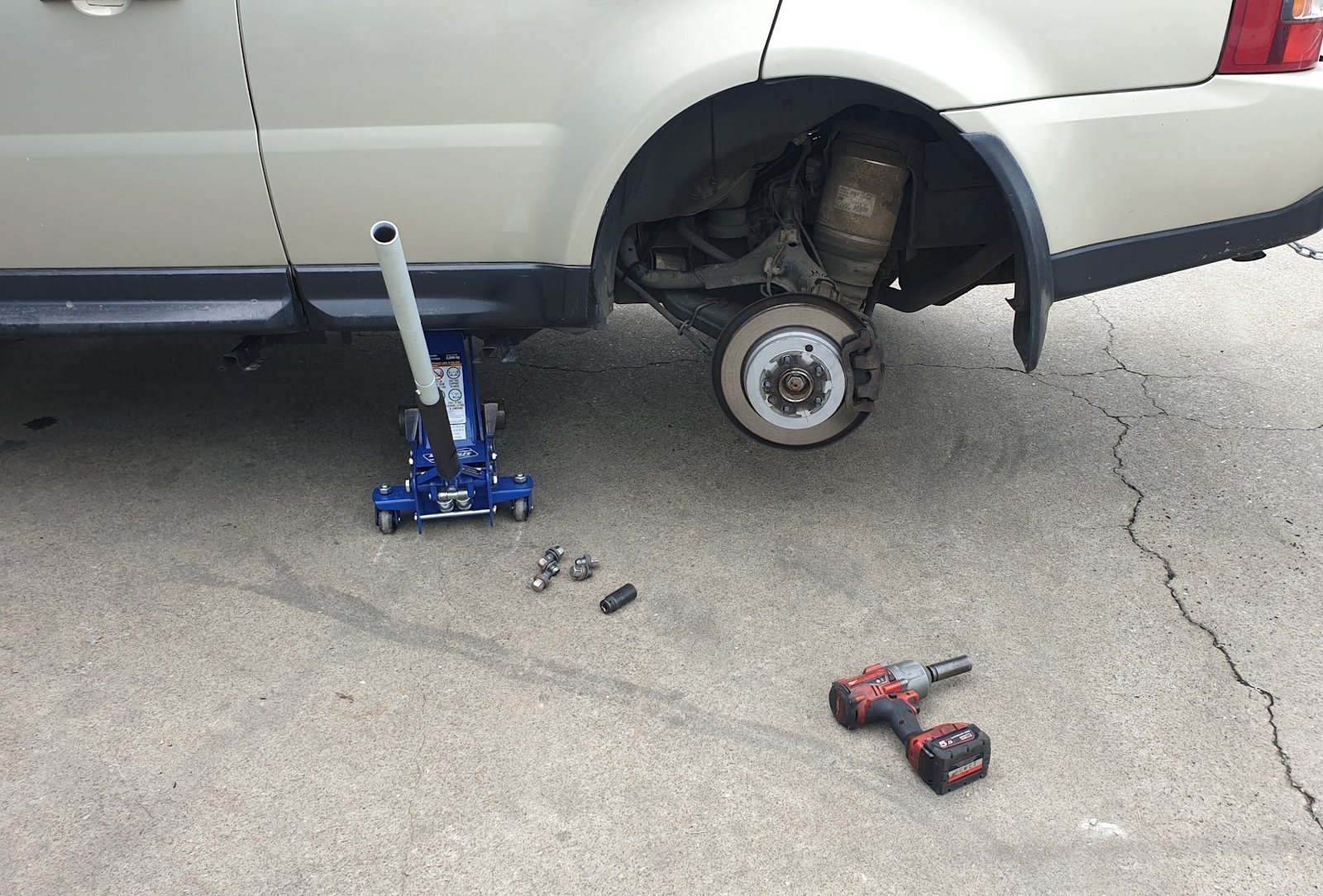 Rear wheel off a four wheel drive, brake disc exposed, trolley jack and rattle gun on the concrete