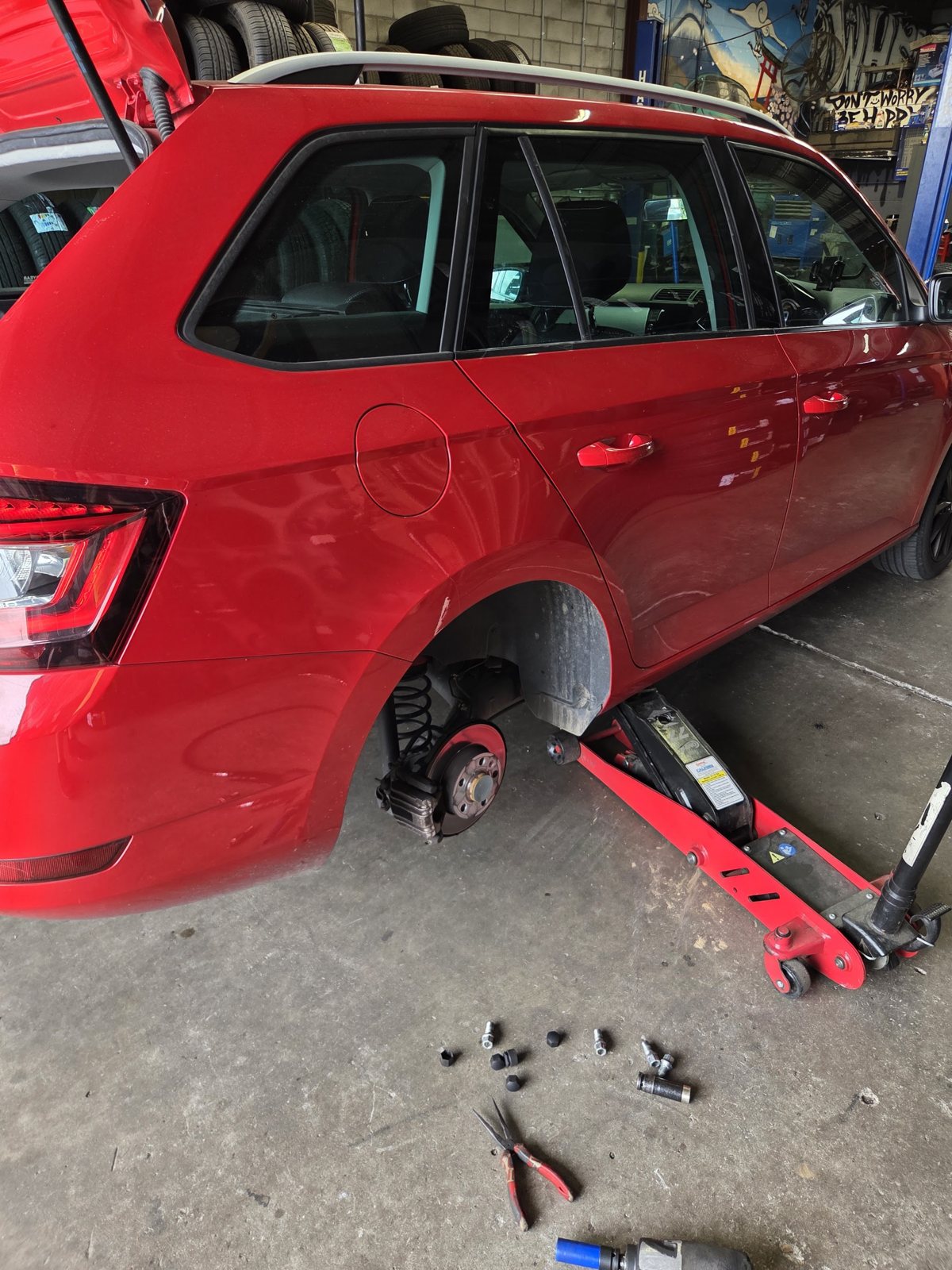 Red wagon up on a trolley jack inside the workshop with its rear wheel removed