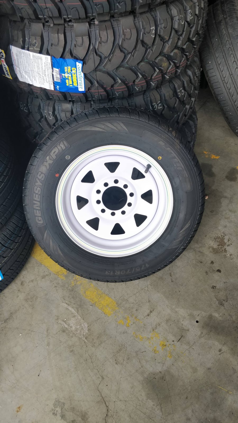 New tyre fitted to a white steel wheel, stacked against more new tyre stock